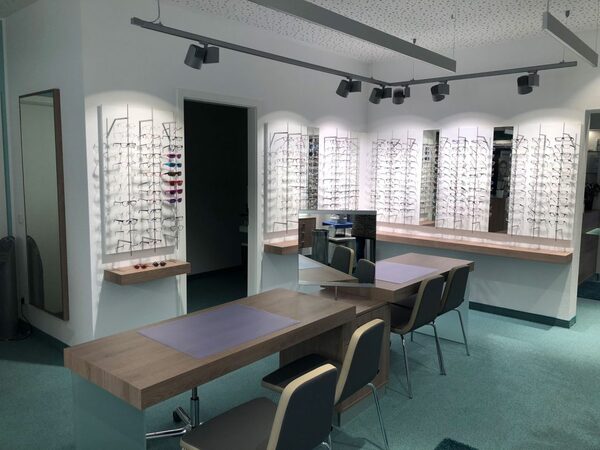 Moderner Optikerladen mit Beratungstischen und großer Auswahl an Brillenfassungen.